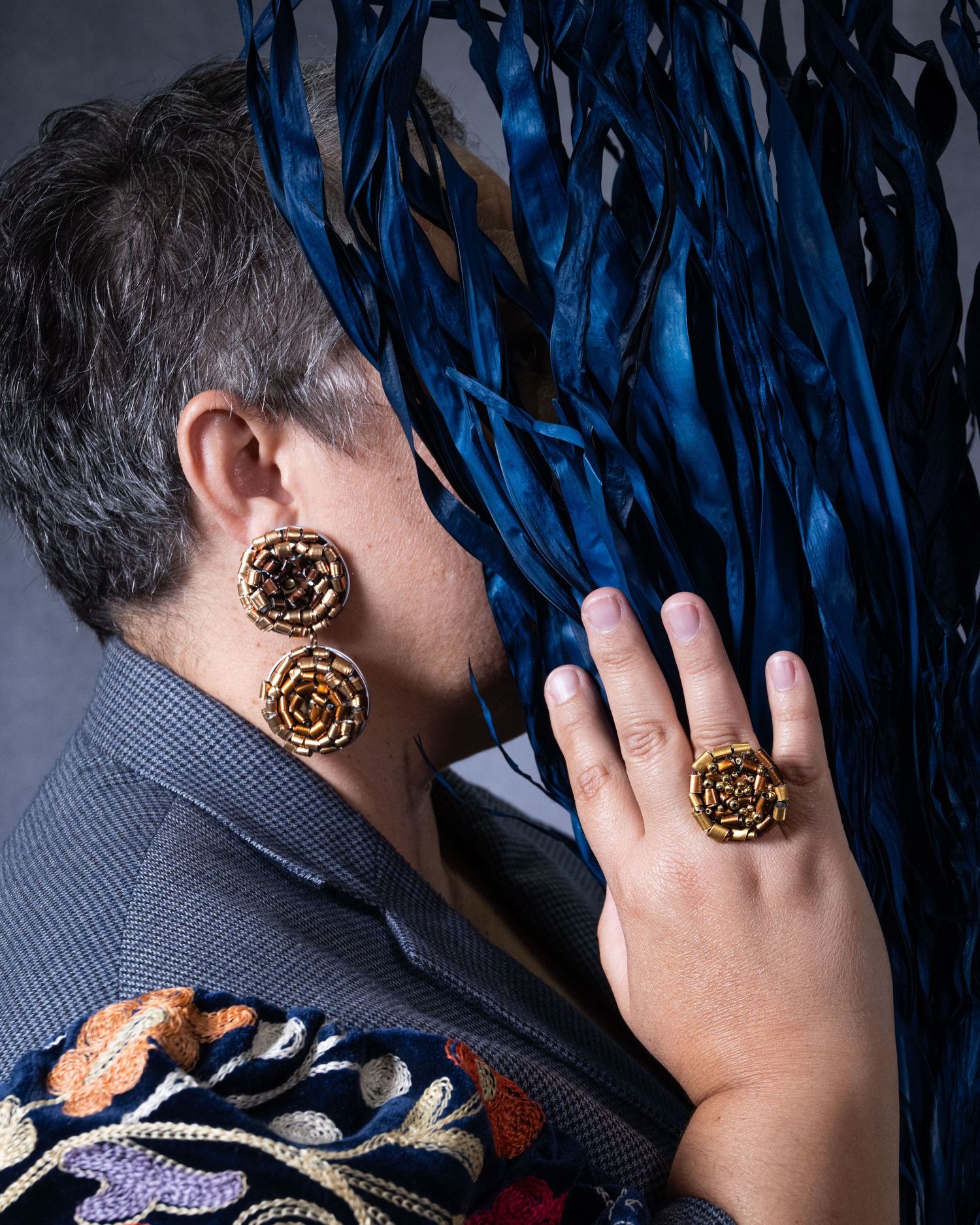 A women whose face is obscured by a deep blue plant, wearing a matching set of earrings and jewelry.