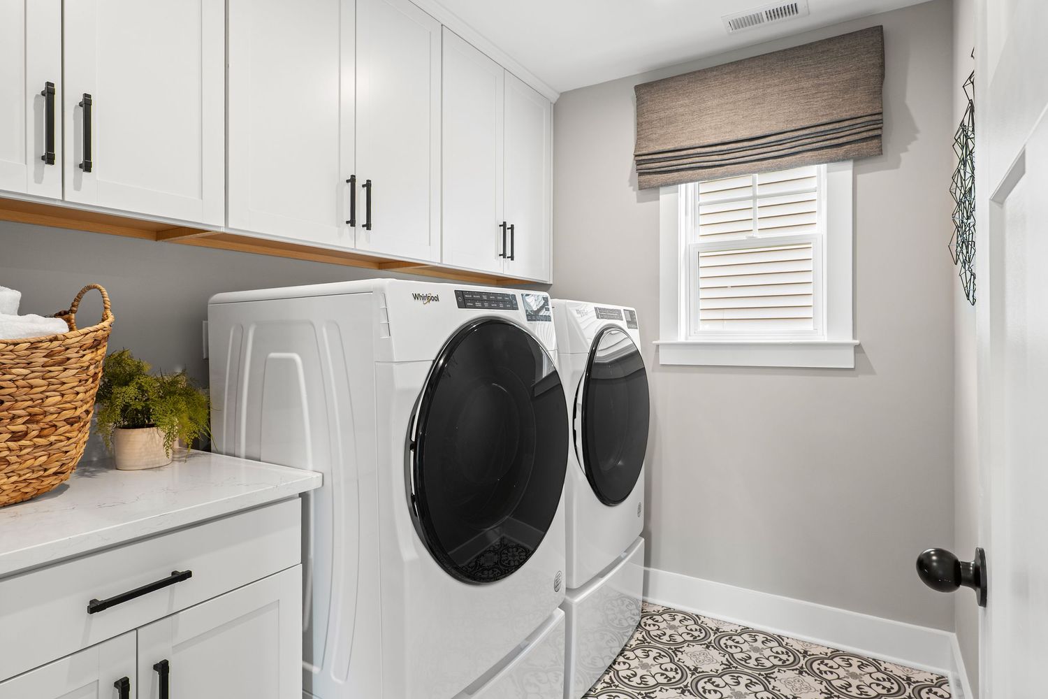 Modern laundry room with white cabinets, side-by-side washer and dryer, and patterned floor tile.