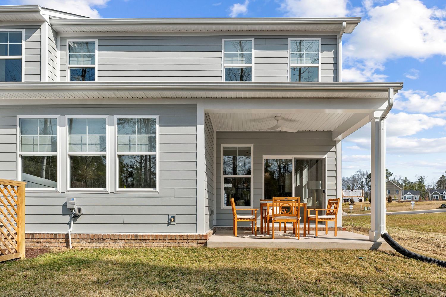 Spacious covered porch with wooden furniture overlooking expansive backyard on gray house.