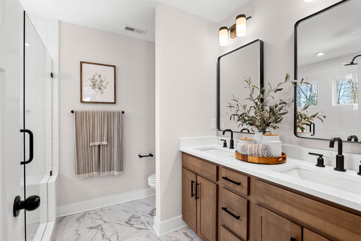 Luxurious bathroom featuring marble floors, double vanity with wood cabinets and frameless shower.
