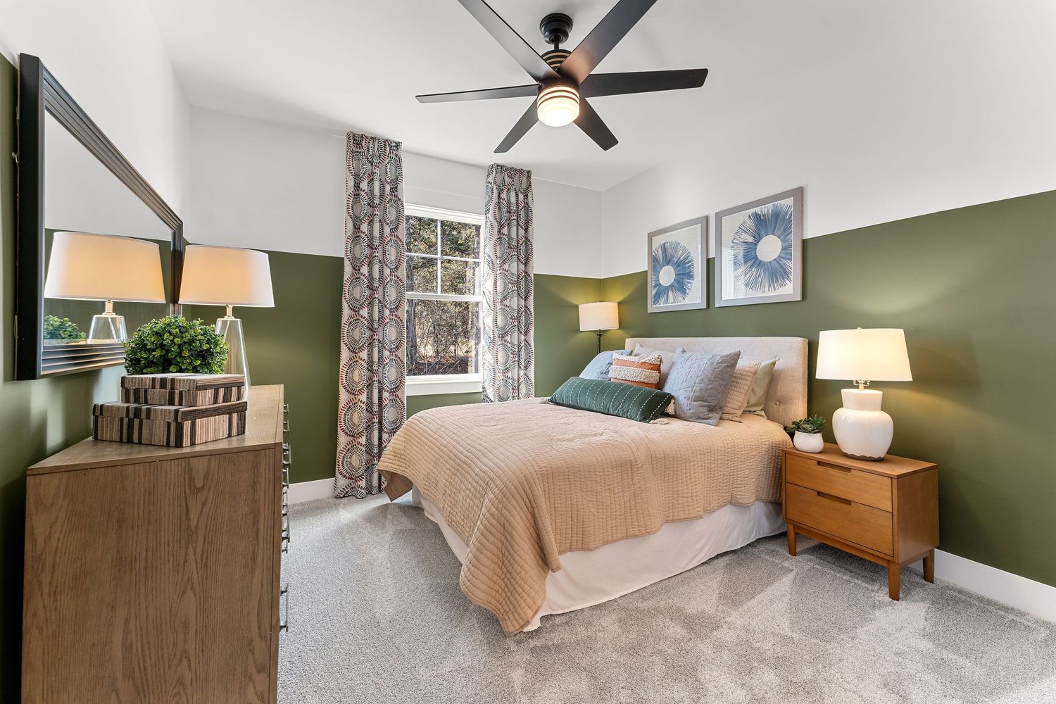 Modern bedroom with olive green accent walls, beige bedding, wooden furniture, and a ceiling fan.