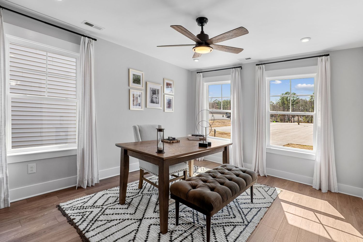 Open concept living space with ceiling fan, area rug, and large windows letting in natural light.
