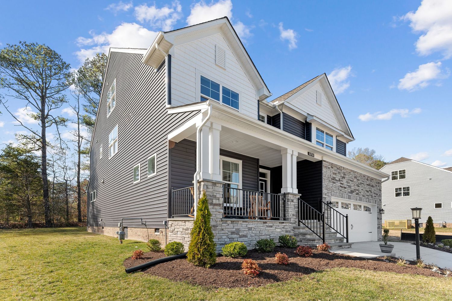 Modern two-story home with gray siding, covered front porch, and fresh landscaping against blue sky background.