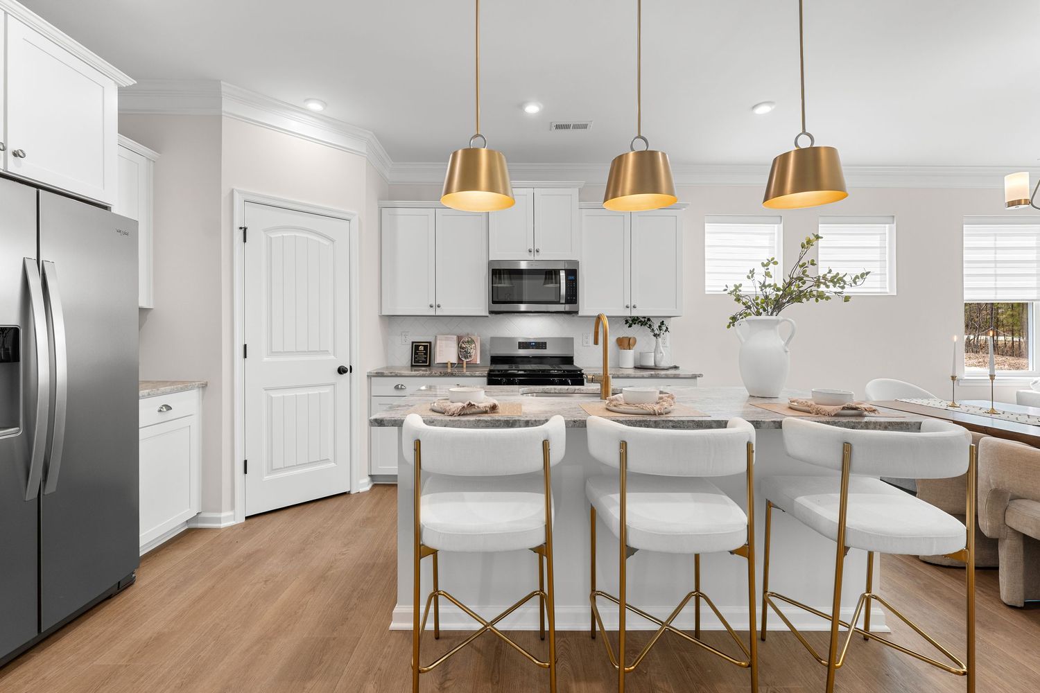 White modern kitchen with gold pendant lights, marble countertops, and bar seating.