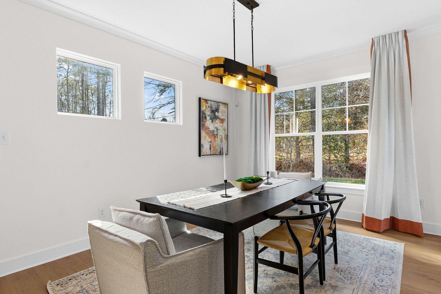 Modern dining area with dark wood table, mixed seating, and a contemporary gold pendant light fixture near large windows.