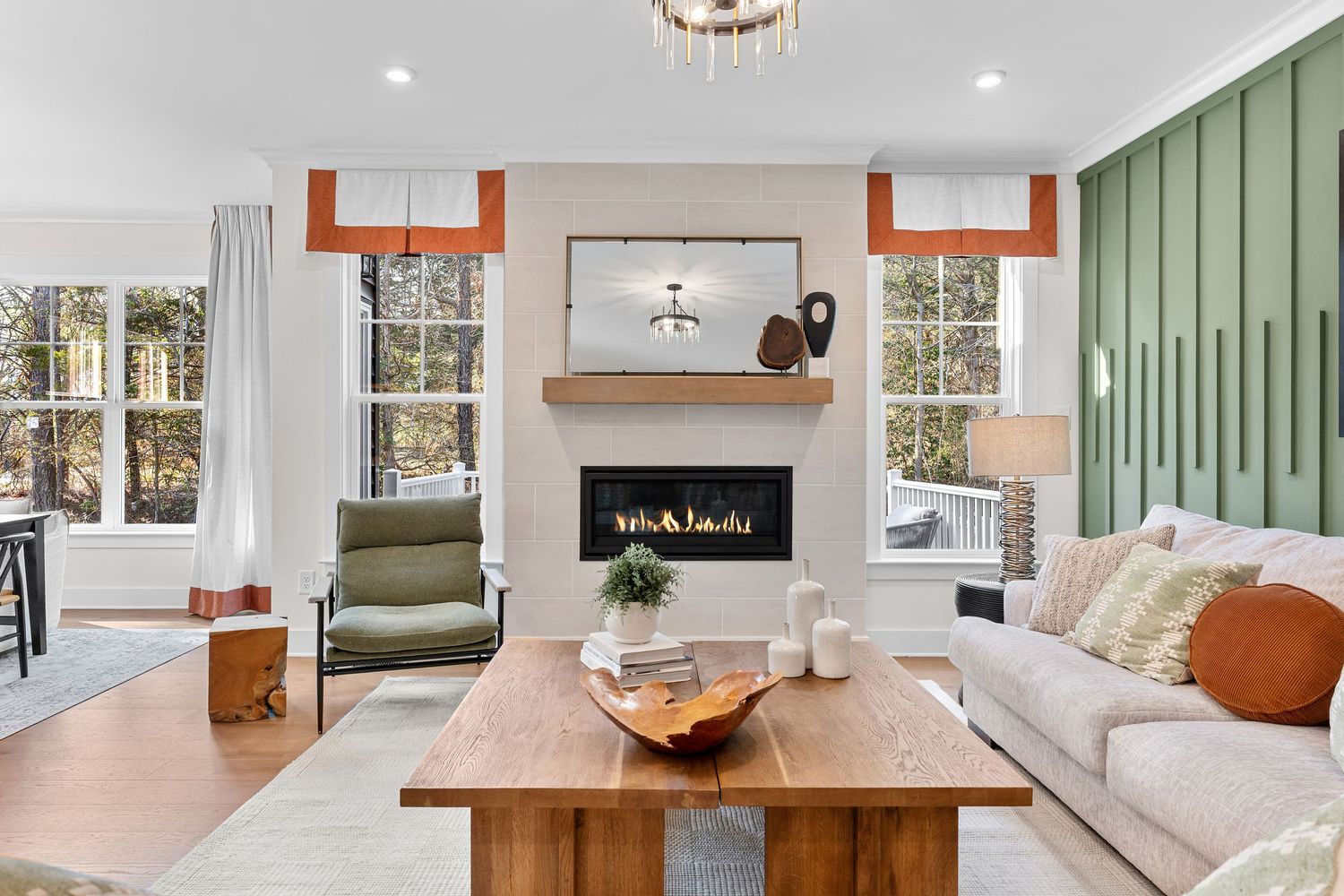 Modern living room features sage green paneled walls, white trim, and warm wood accents with comfortable seating.