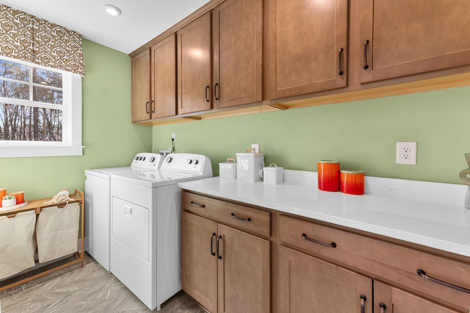 Modern kitchen with brown cabinets, green walls, white countertops and stainless steel appliances in a bright space.
