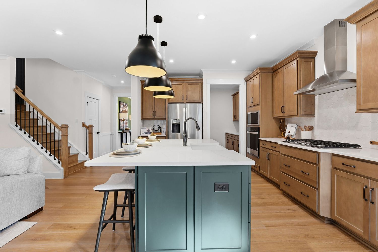 Modern kitchen with wood cabinets, teal island, white countertops, pendant lights and hardwood floors in open concept space.