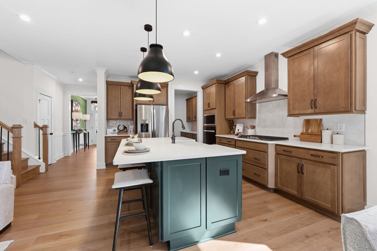 Modern kitchen with wood cabinets, white countertops, and hardwood floors features pendant lighting and stainless appliances.