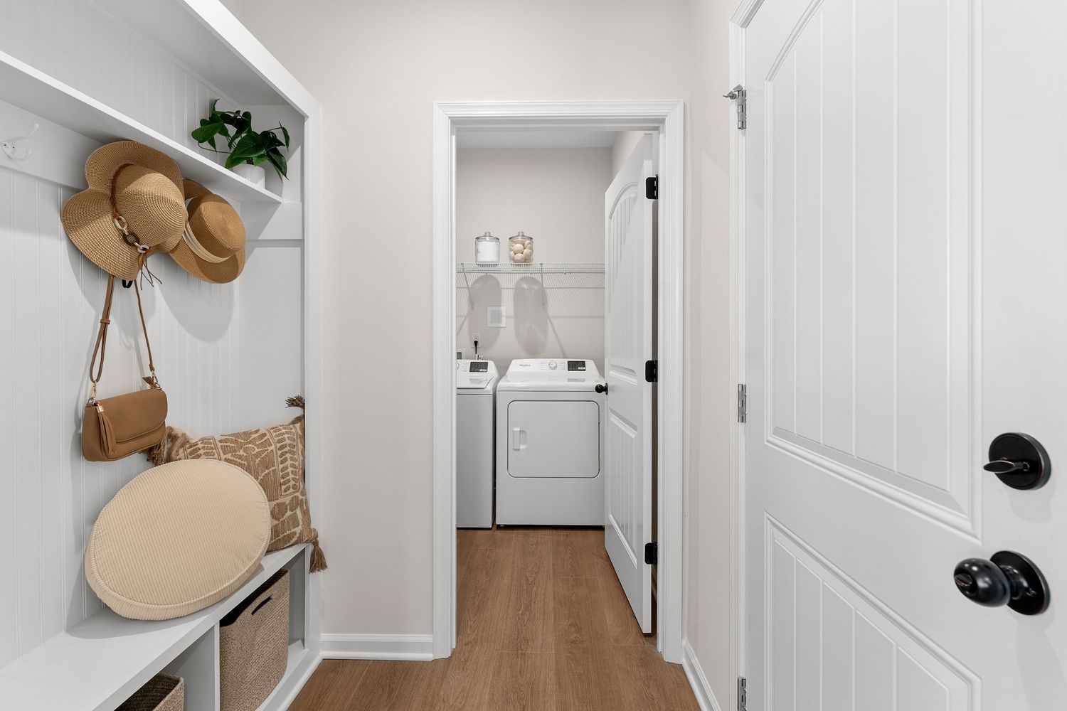 Mudroom hallway with built-in bench, wall hooks for storage, and hardwood flooring.