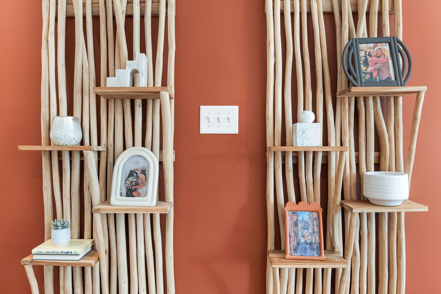 Vertical wooden dowels mounted on a coral-colored wall create a modern decorative display with floating shelves.