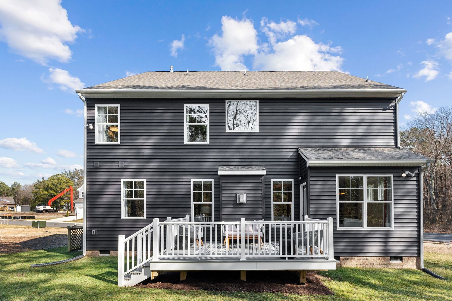 Modern two-story gray house with white trim and large back deck under bright blue sky with puffy clouds.
