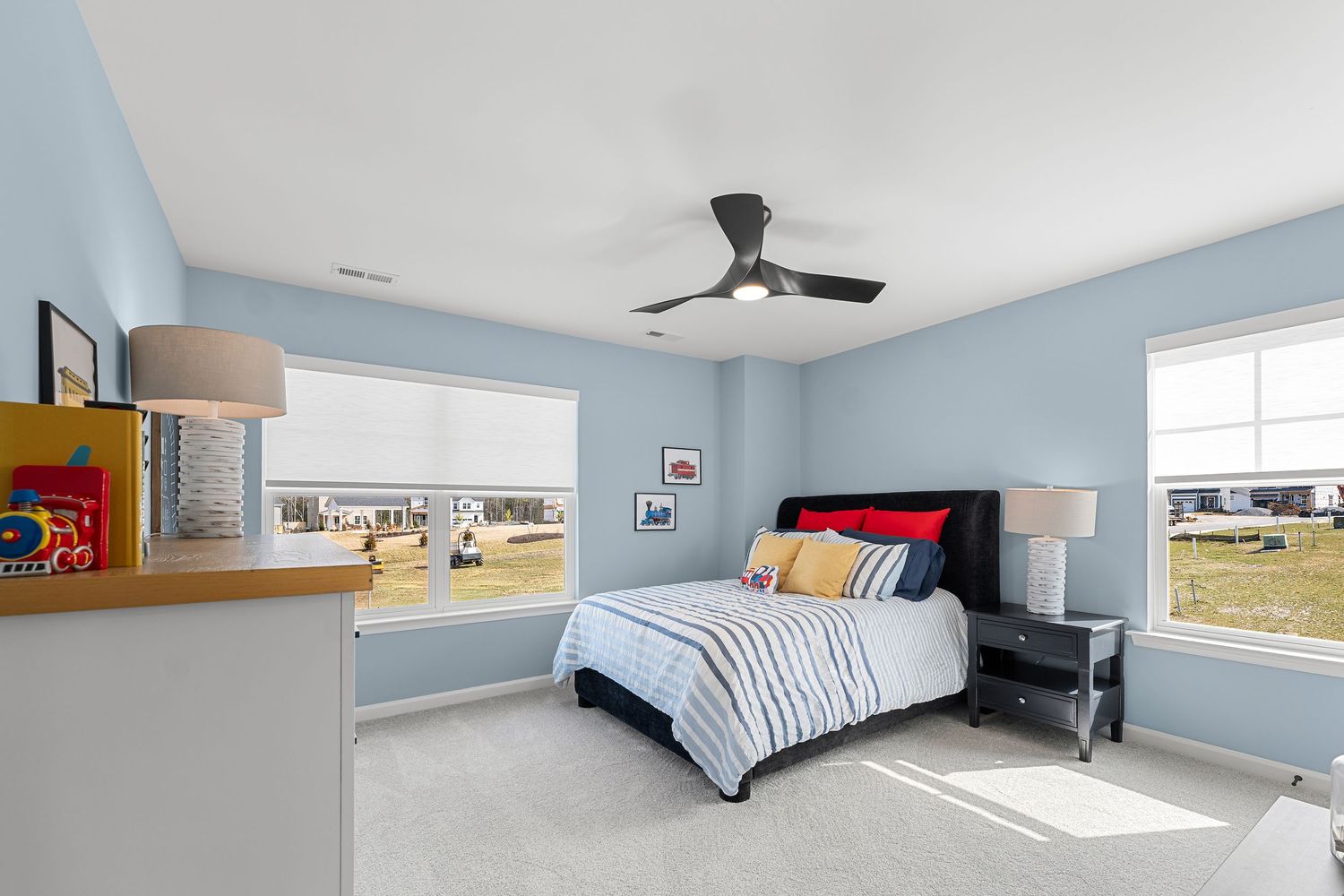 Airy bedroom with light blue walls, ceiling fan, and large windows providing natural illumination.