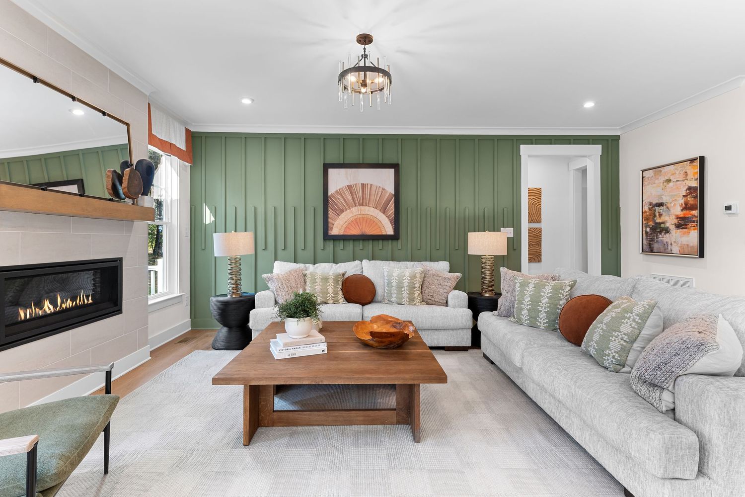 Modern living room with sage green accent wall, gray sectional sofa, wooden coffee table and contemporary wall-mounted fireplace.