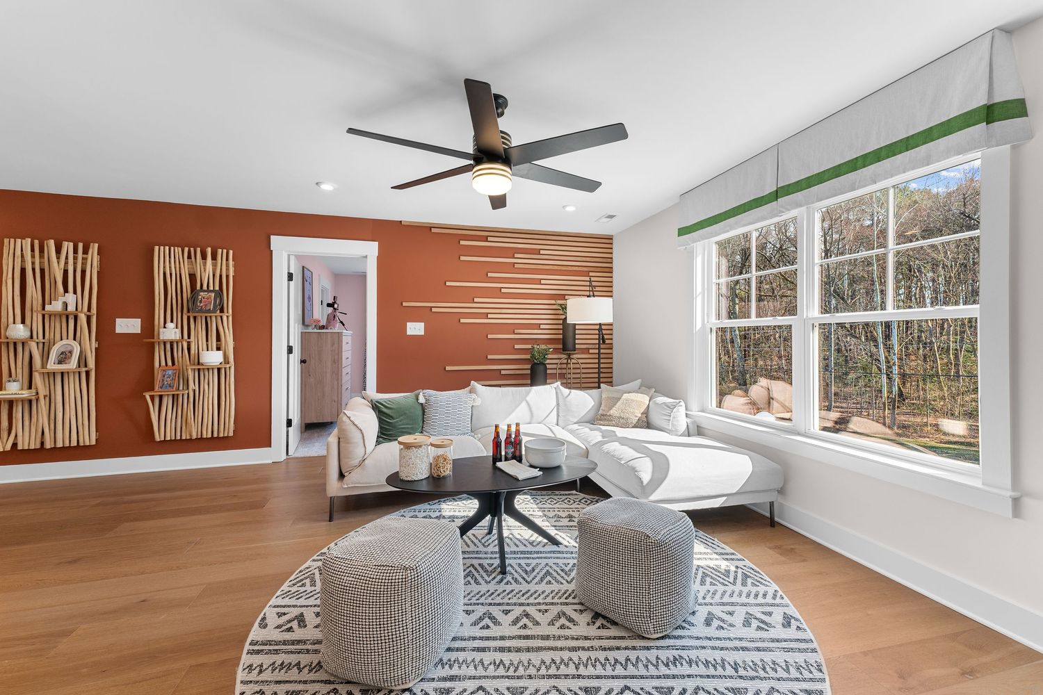Modern living room with wood accent wall, white sectional sofa, geometric rug, and large windows with natural light.