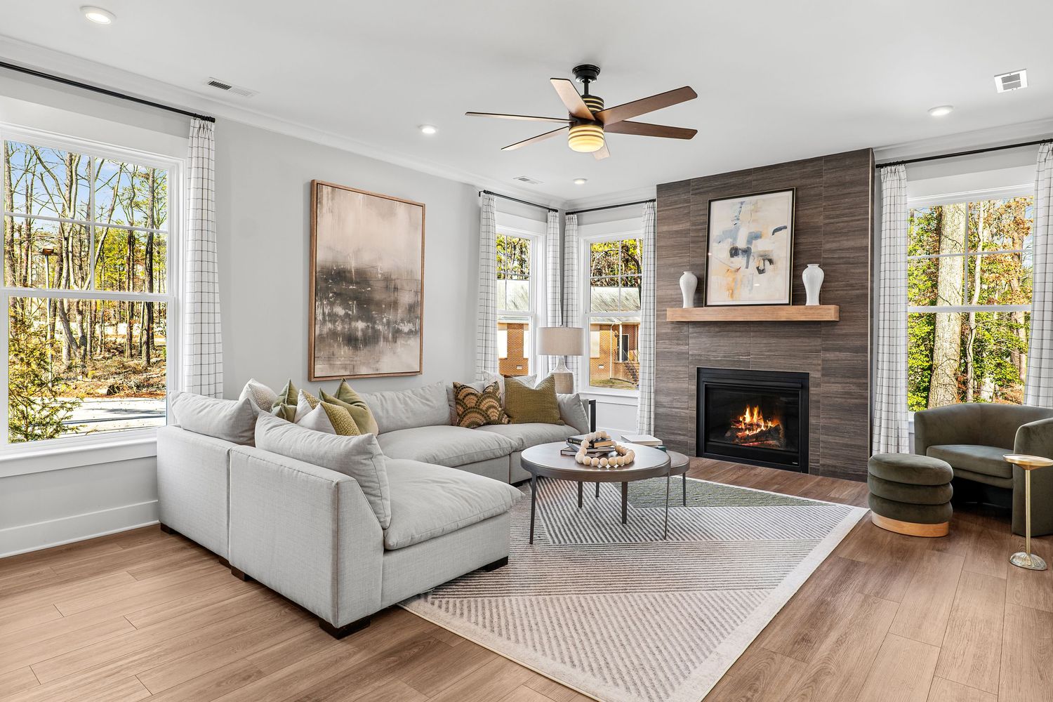 Open concept living room with hardwood floors, white furniture, and large windows overlooking natural scenery.