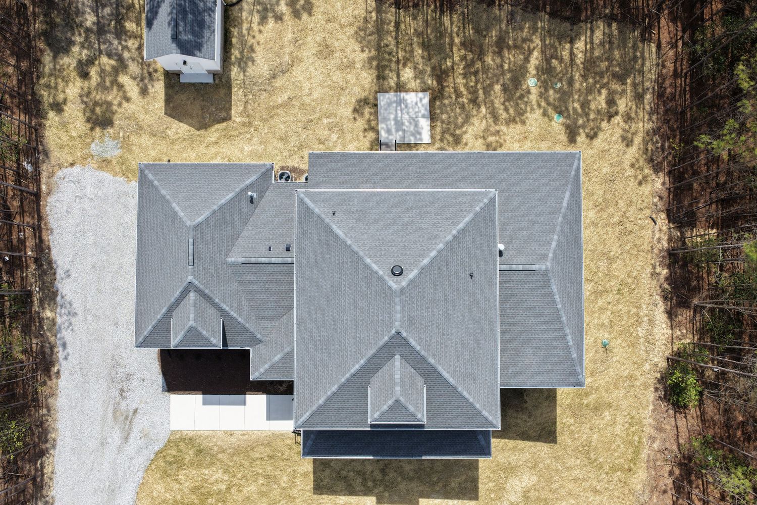 Aerial view of a modern residential house with a gray multi-level roof and beige yard seen from directly above.