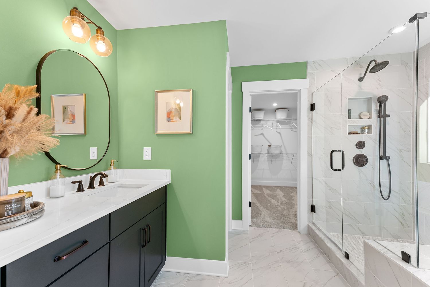 Modern bathroom with mint green walls, black vanity, round mirror, and glass shower enclosure featuring white marble tile details.