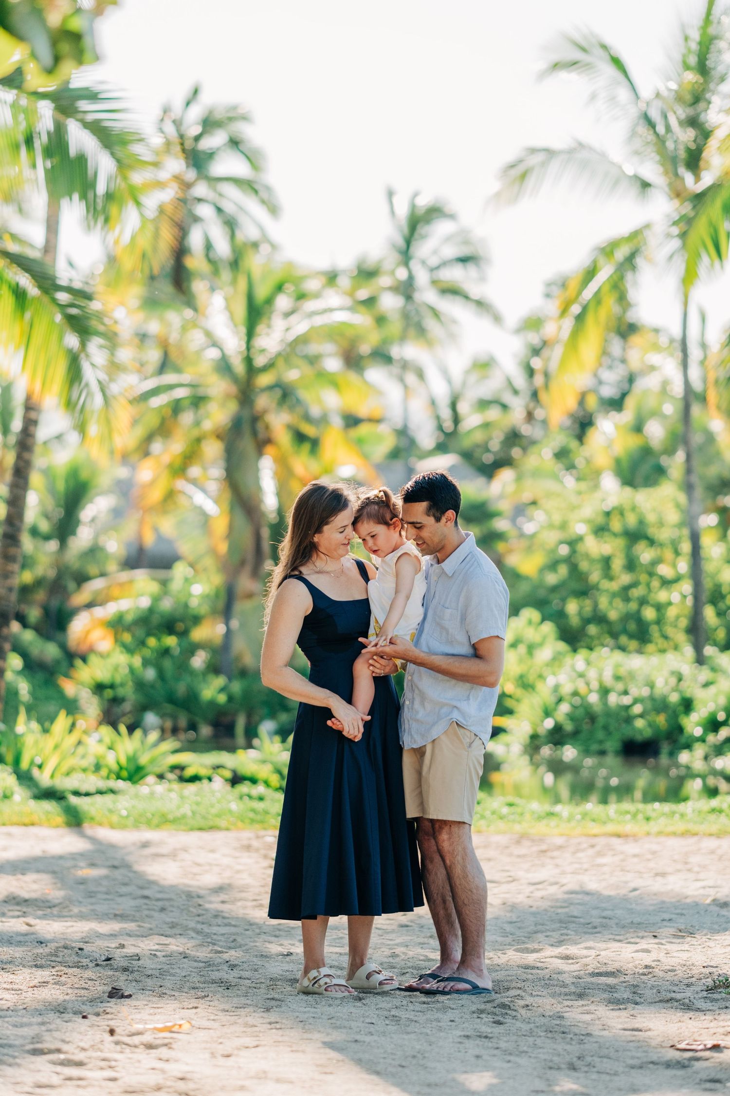 Family sharing tender moments among palm trees on a tropical beach at Kona Village Resort, Big Island of Hawaii.