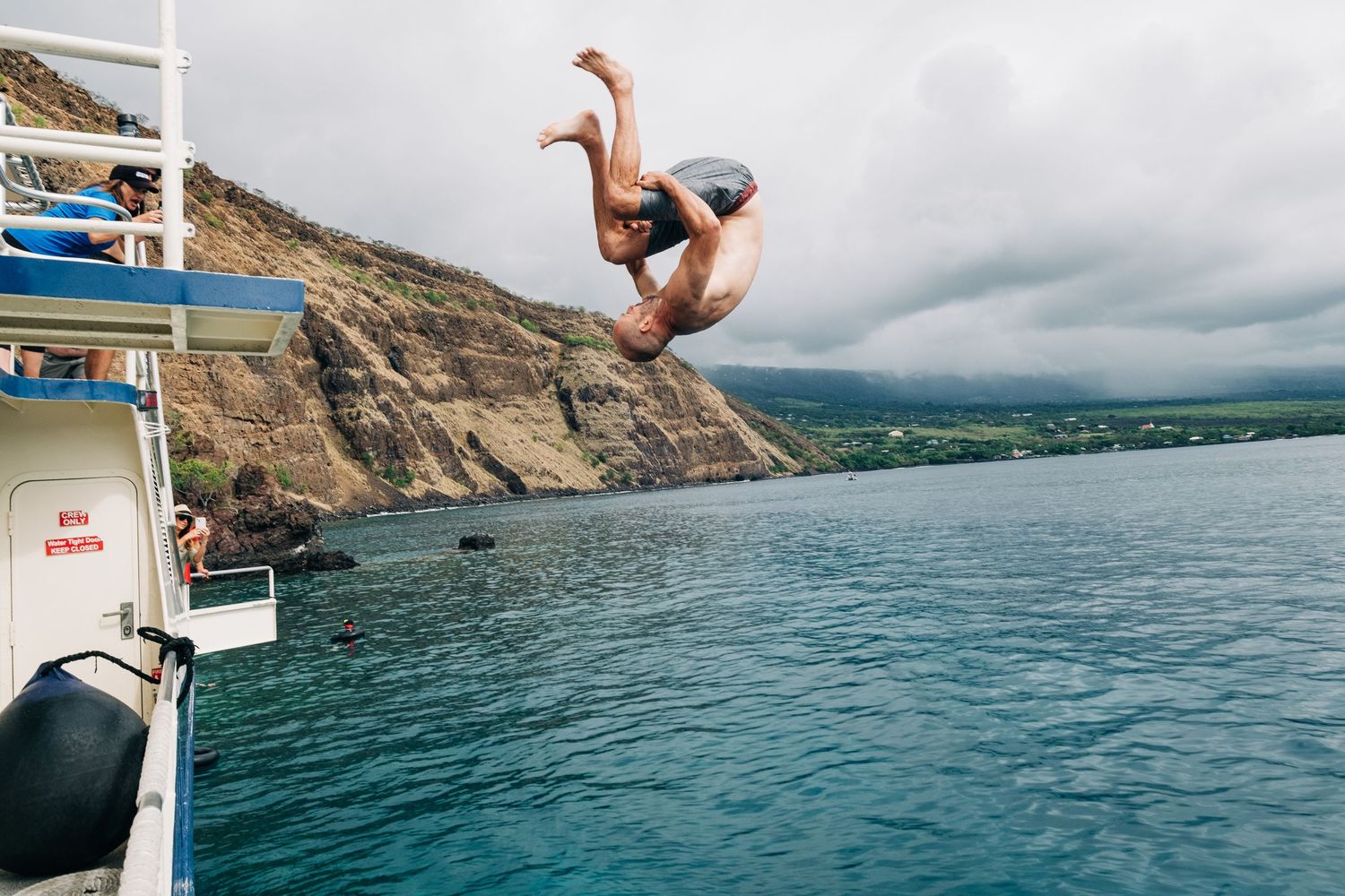 Person diving into blue ocean water from a boat near rocky coastal cliffs in Kona, Big Island of Hawaii.