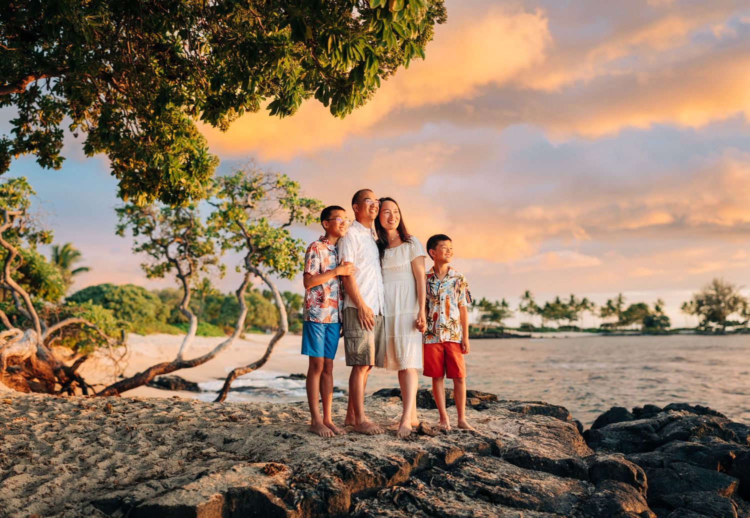 Family group poses together on rocky beach during golden sunset in Hawaii at Kukio Beach, Kona, Big Island Hawaii.