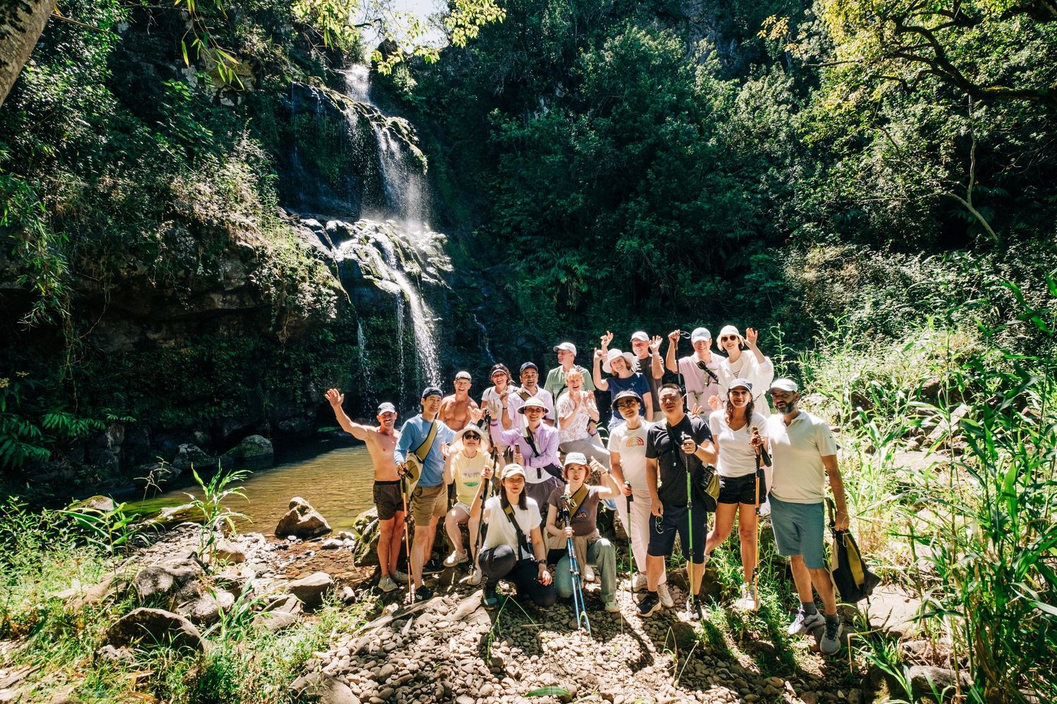 A group explores a scenic waterfall and rocky terrain surrounded by lush greenery on the Big Island of Hawaii.