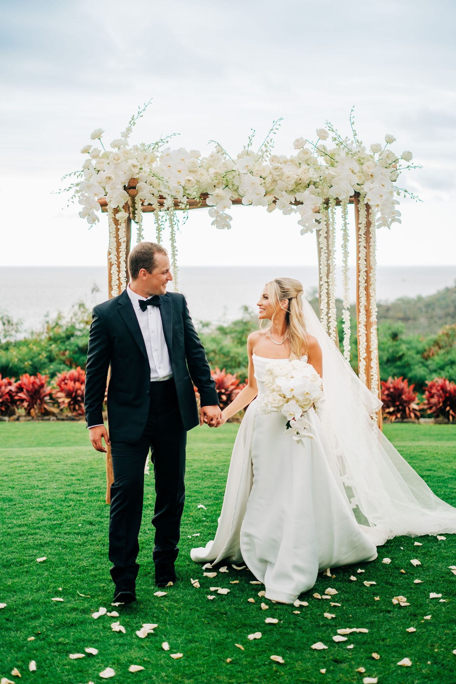 Elegant outdoor wedding ceremony with floral arch and white decor on manicured lawn. Kohanaiki wedding in Kona, Big Island.