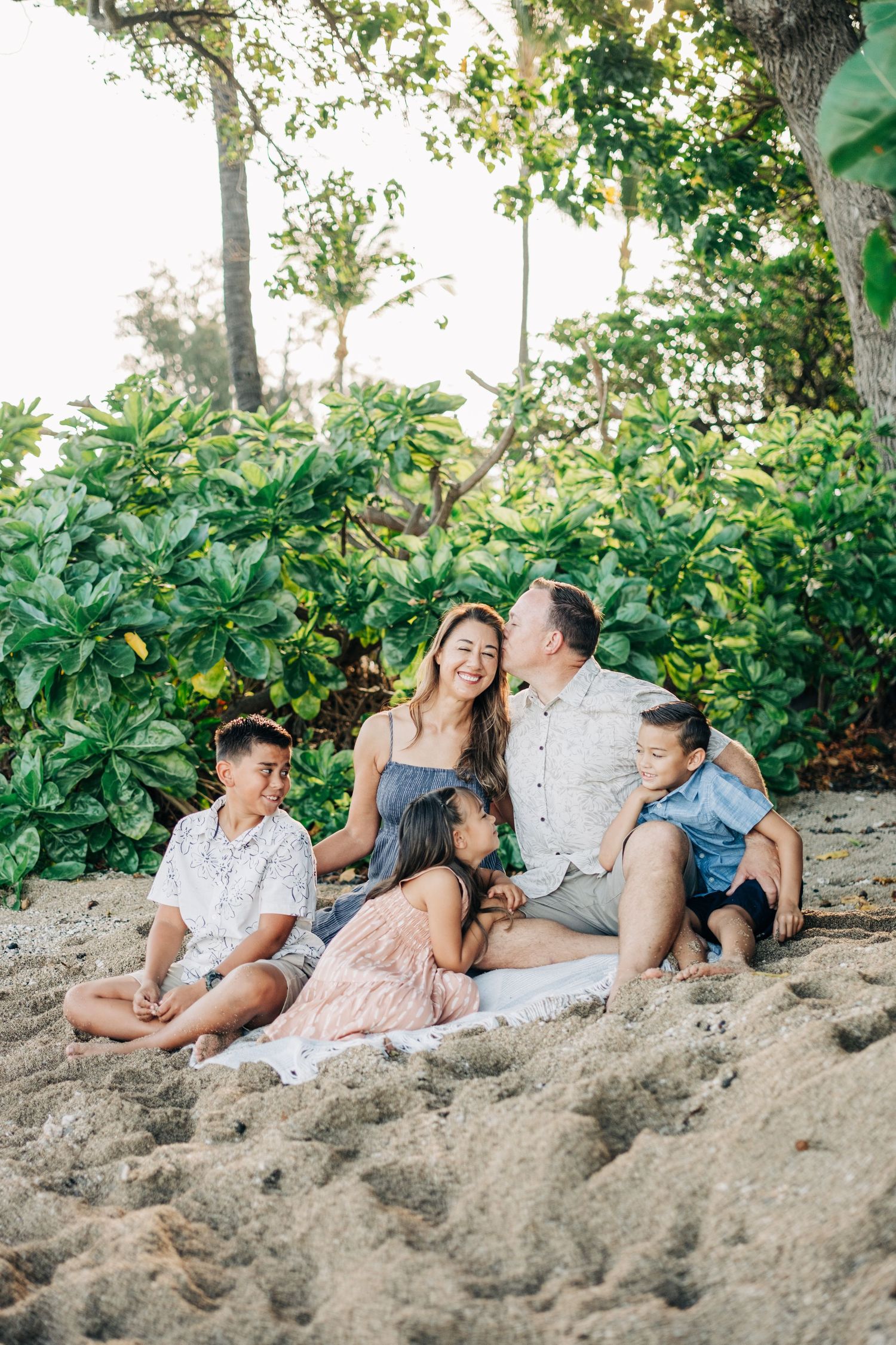 Family relaxing together on a tropical beach with lush greenery in the background at Puako, Big Island Hawaii.