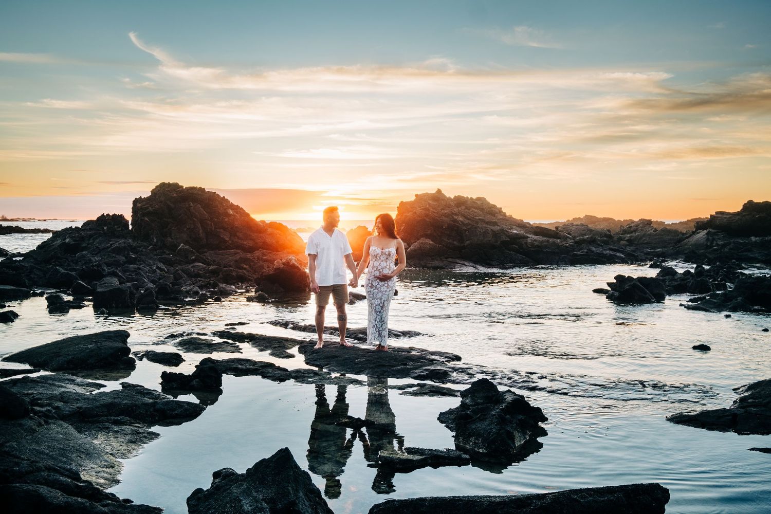 Silhouetted figures on rocky beach landscape during golden hour sunset at Kikaua Point Beach, Big Island of Hawaii.