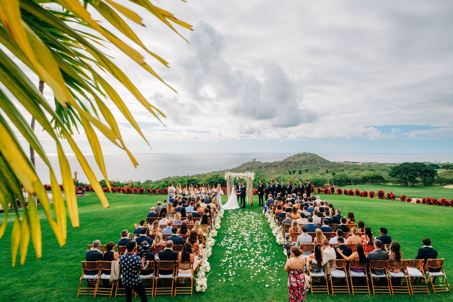 Outdoor wedding ceremony setup with wooden chairs on lush green Hawaiian hillside. Kohanaiki wedding in Kona, Big Island.