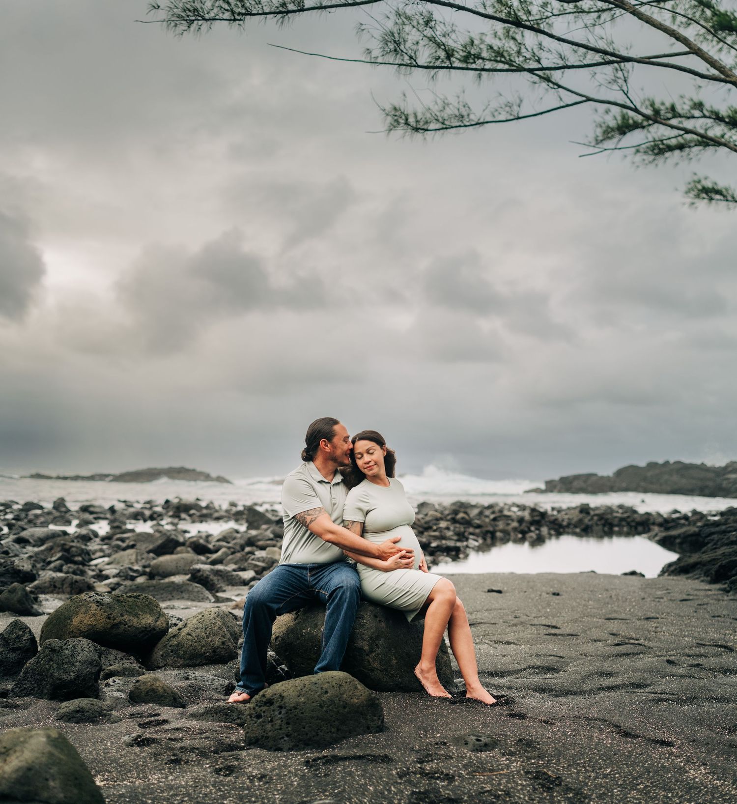 Romantic couple's portrait session on black sand beach with moody sky in Hilo, Big Island Hawaii.