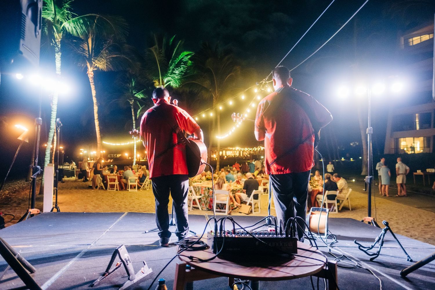 Nighttime outdoor event with stage lighting and string lights under palm trees at a Mauna Lani Beach Resort event.