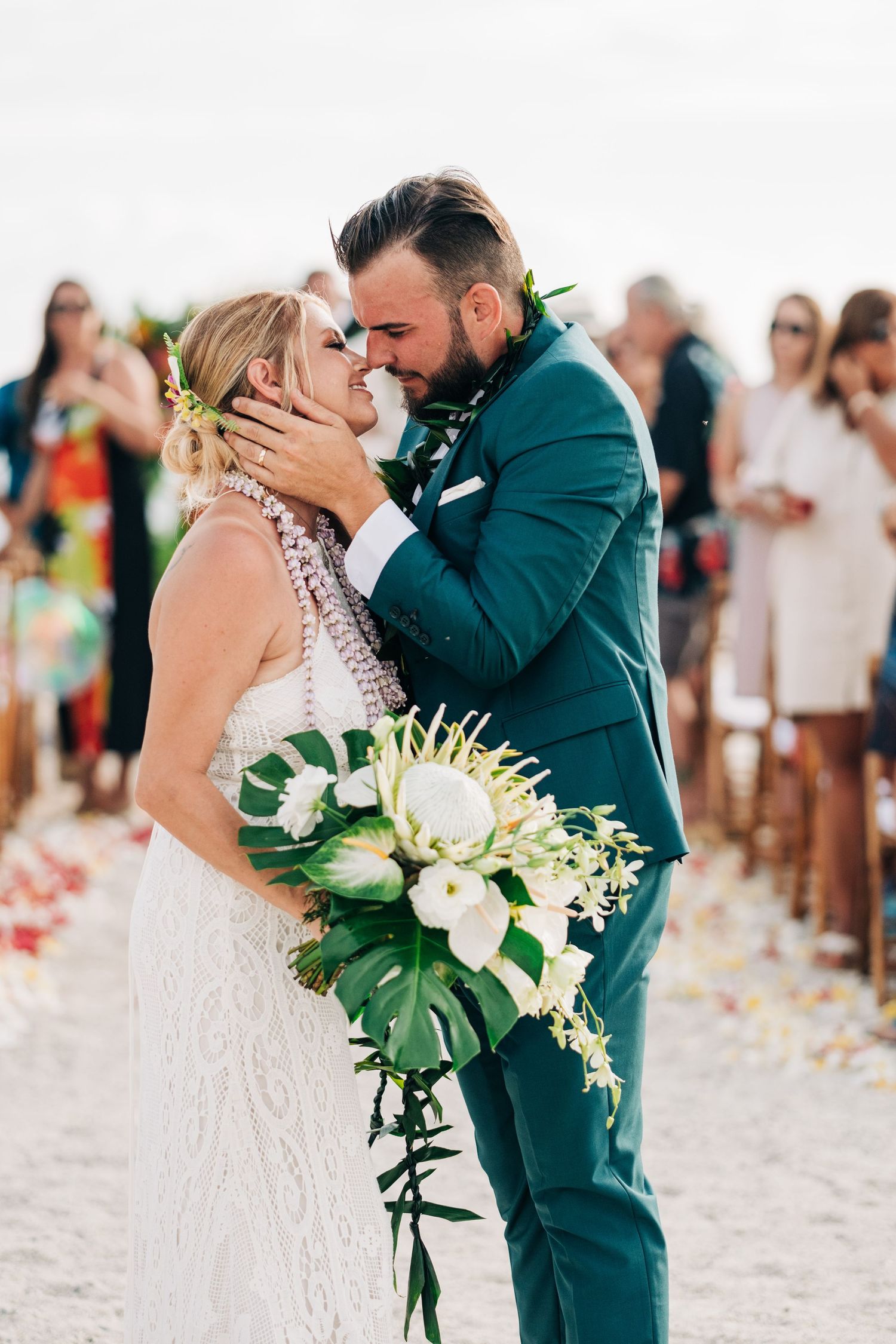 Intimate moment between couple under tropical floral arch during beach wedding ceremony at Kona Salt Farm, Big Island Hawaii.