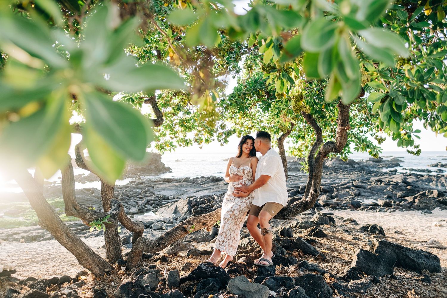 Romantic couple's photoshoot under tropical trees near a Hawaiian beach at Kikaua Point Beach, Big Island of Hawaii.