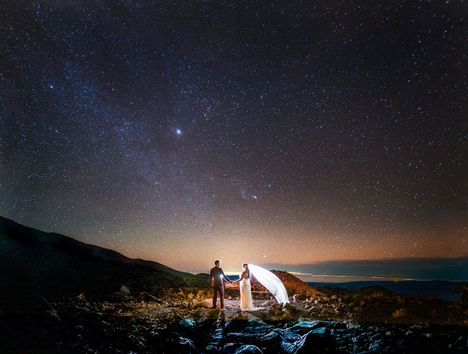 Camping tent illuminated under a starry night sky with mountains in the background on Mauna Kea, Big Island Hawaii.