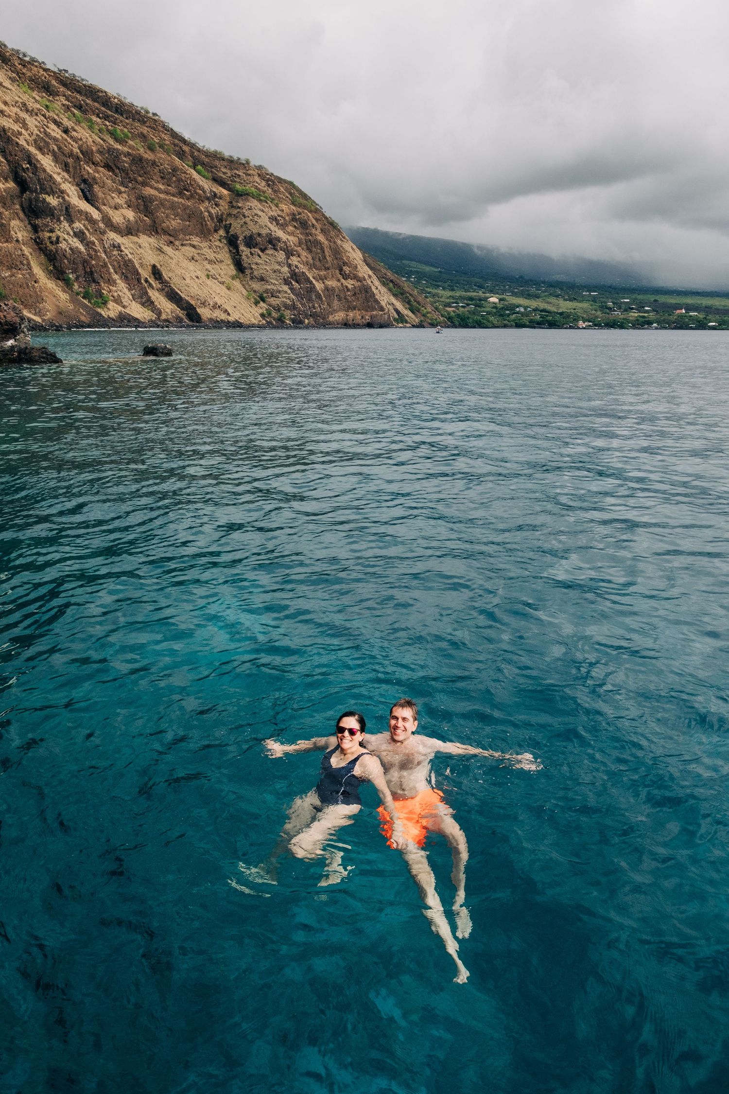 Two people floating in turquoise ocean waters near dramatic coastal cliffs, Kona Big Island of Hawaii.