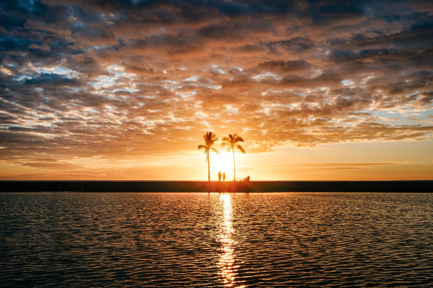 Vibrant orange sunset over calm waters with silhouetted palm trees at Waikoloa, Big Island Hawaii.