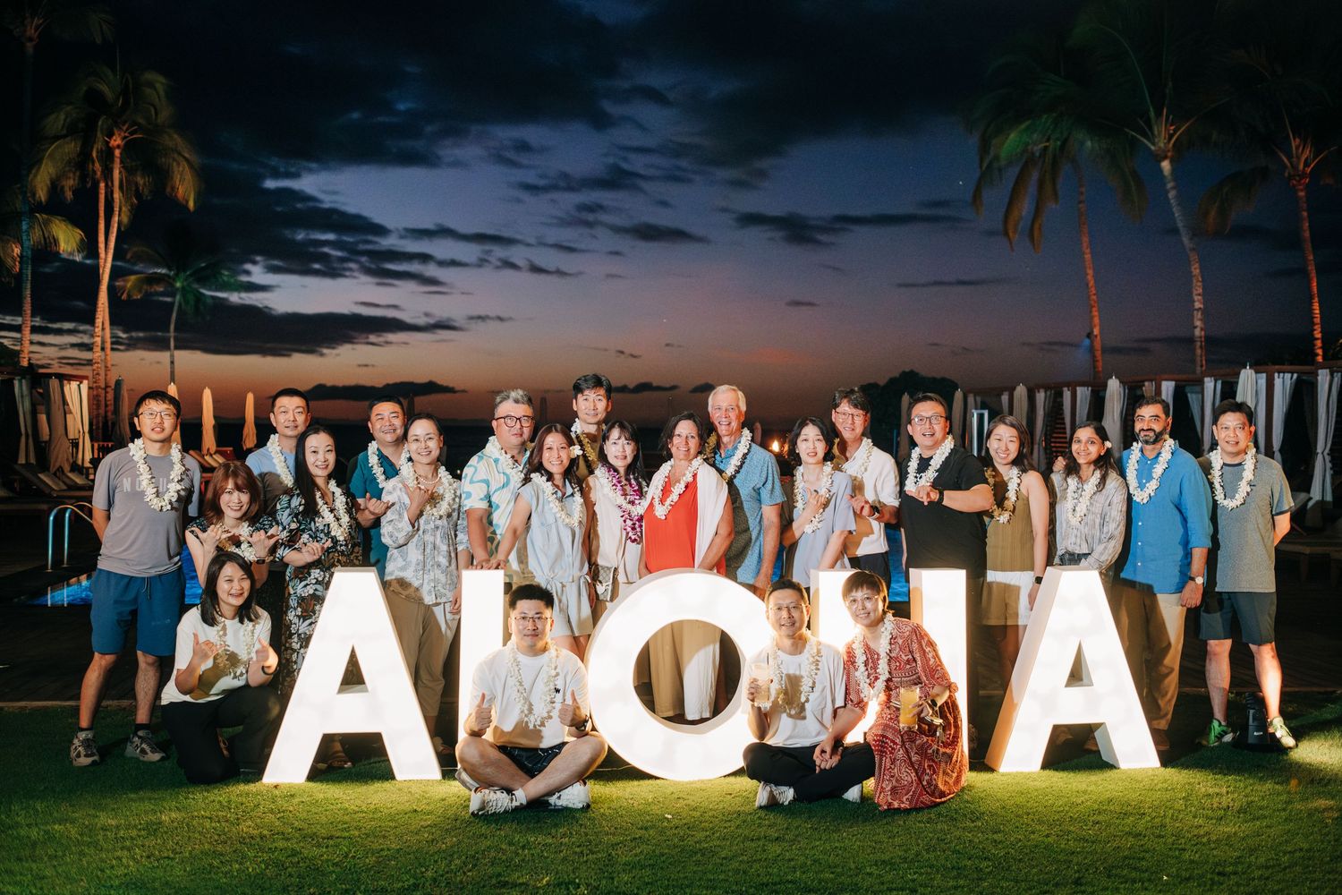 Group photo with large ALOHA letters on a lawn during twilight with palm trees at a Four Seasons Hualalai Event.