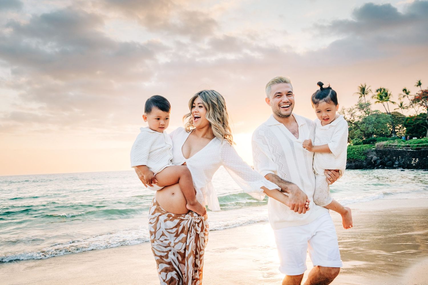 Family plays together on tropical beach at sunset with palm trees at Mauna Kea Beach, Big Island Hawaii.