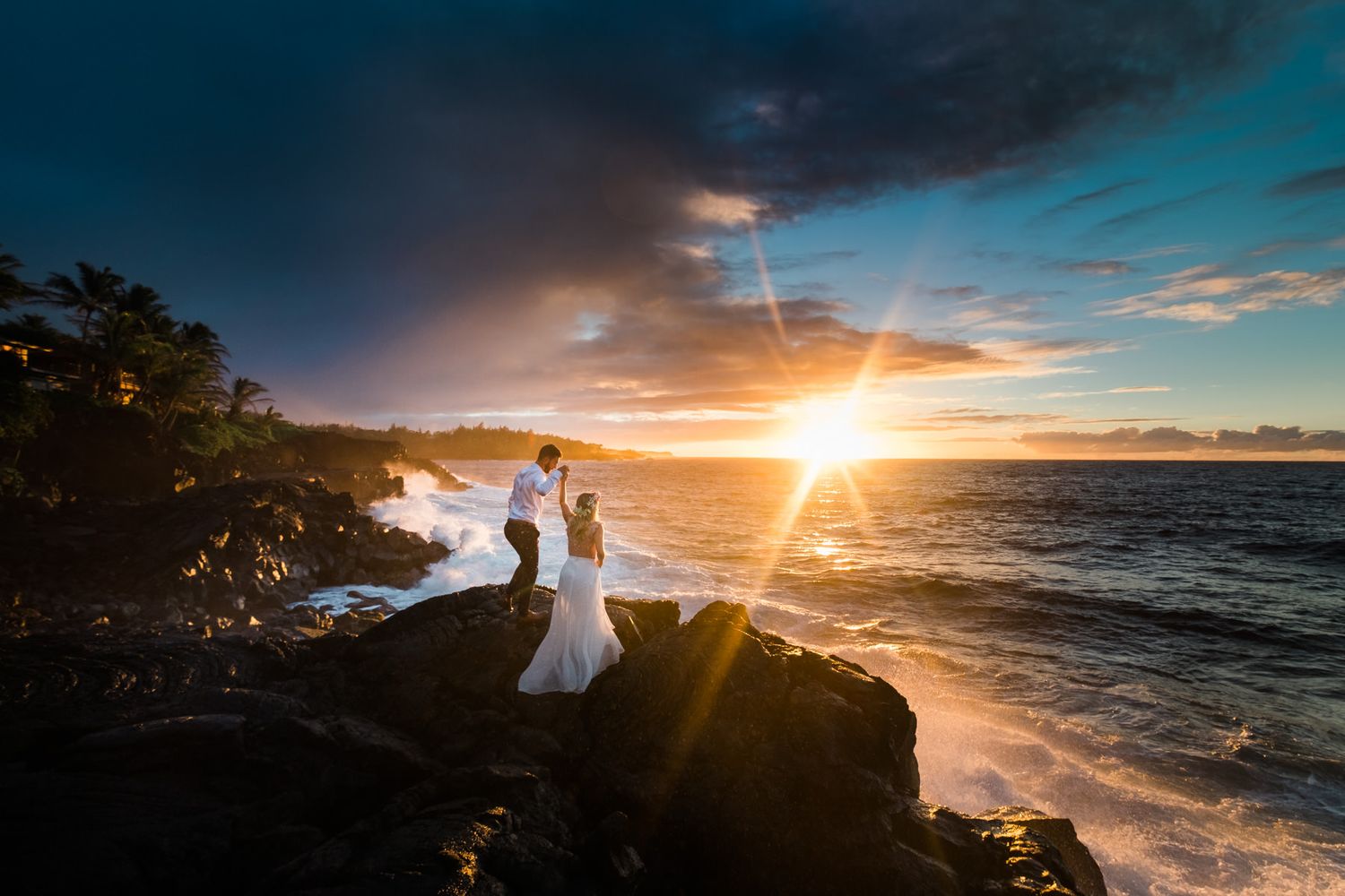 Dramatic silhouettes against fiery Hawaiian sunset with crashing waves and rocky coastline. Big Island, Hawaii.