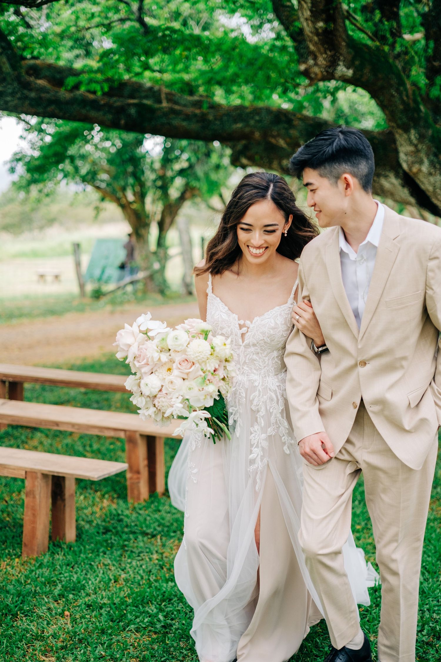 Wedding couple shares intimate moments on lush green grounds with wooden benches at Puakea Ranch, Big Island of Hawaii.