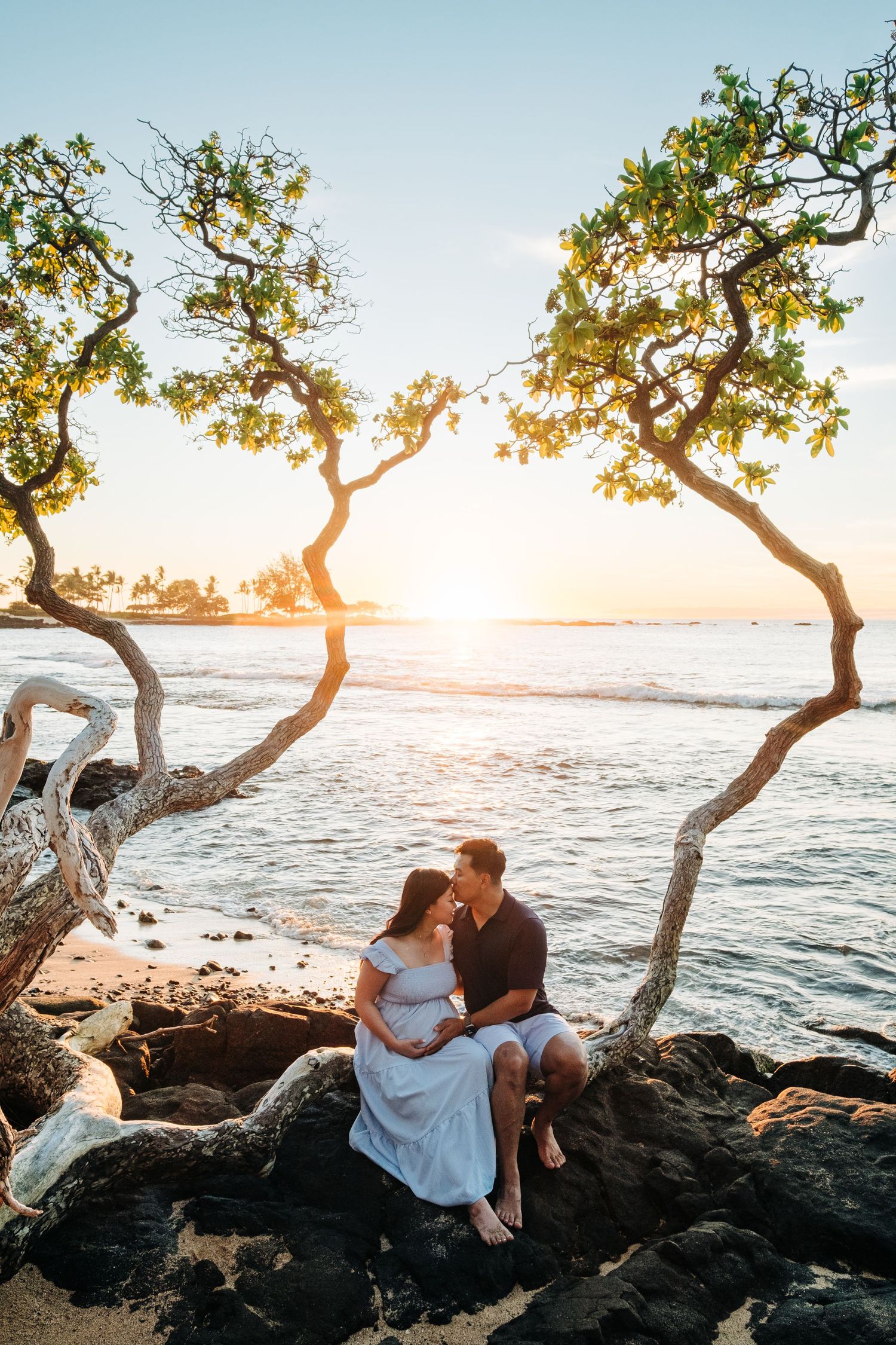 Couple embracing on rocky beach coastline during golden hour sunset at Kukio Beach, Kona, Big Island Hawaii.