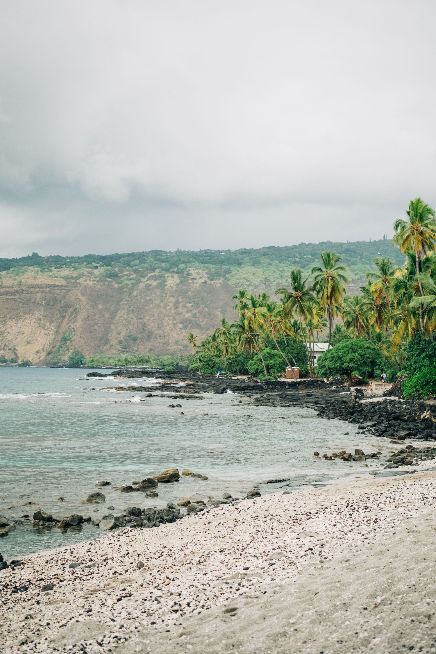 Rocky Hawaiian beach coastline with palm trees and volcanic cliffs in Kona, Big Island of Hawaii.