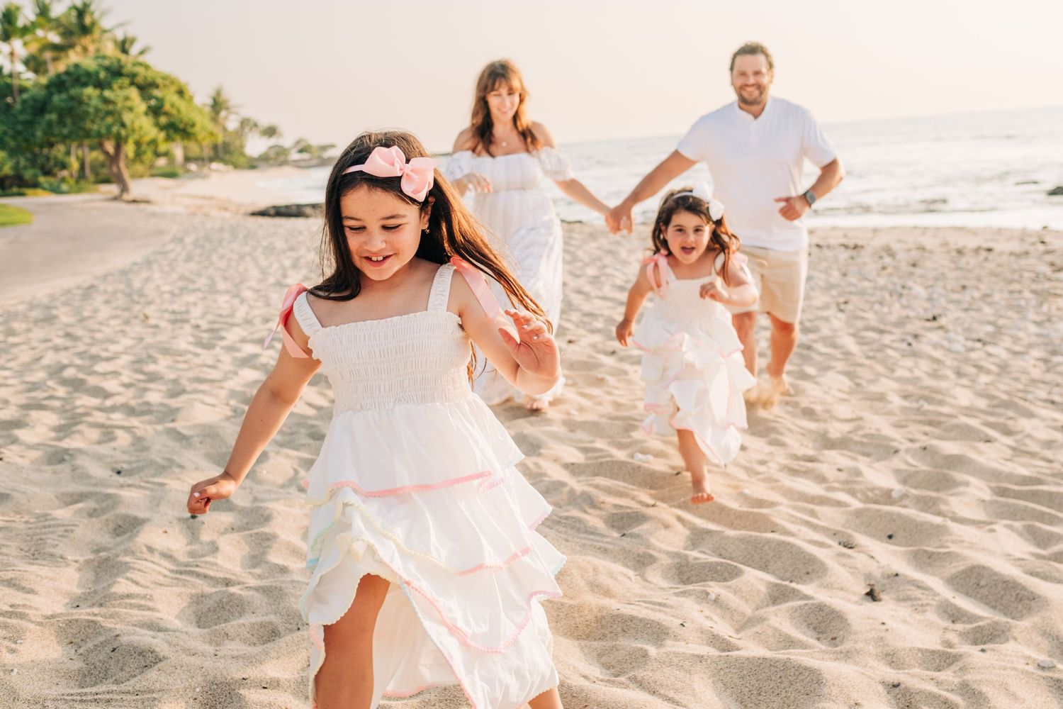 Family running and playing together on a sandy beach in white outfits at Four Seasons Hualalai, Kona, Big Island Hawaii.
