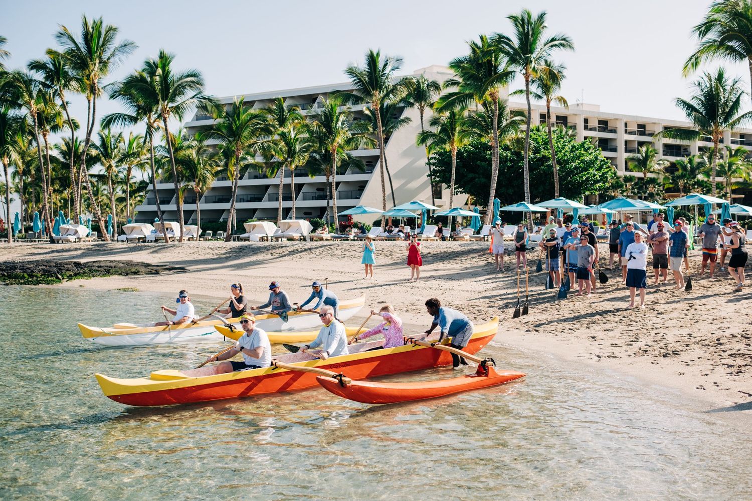 Beach scene with multiple kayaks and paddlers along a tropical Hawaiian shoreline at Mauna Lani Beach Resort.