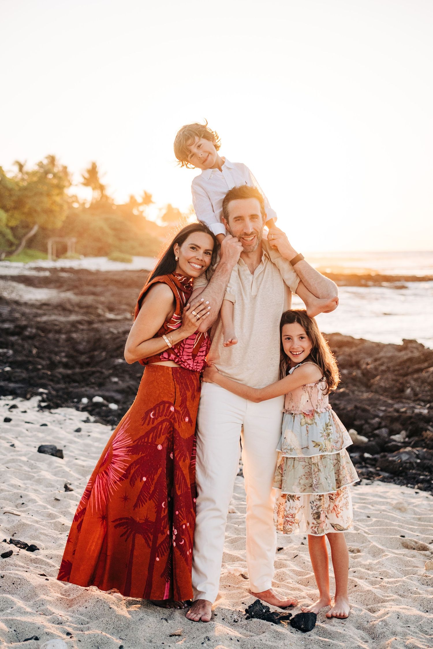 Family enjoying a sunset photoshoot on a sandy beach in Hawaii with volcanic rocks nearby at Kona Village Resort, Big Island Hawaii.
