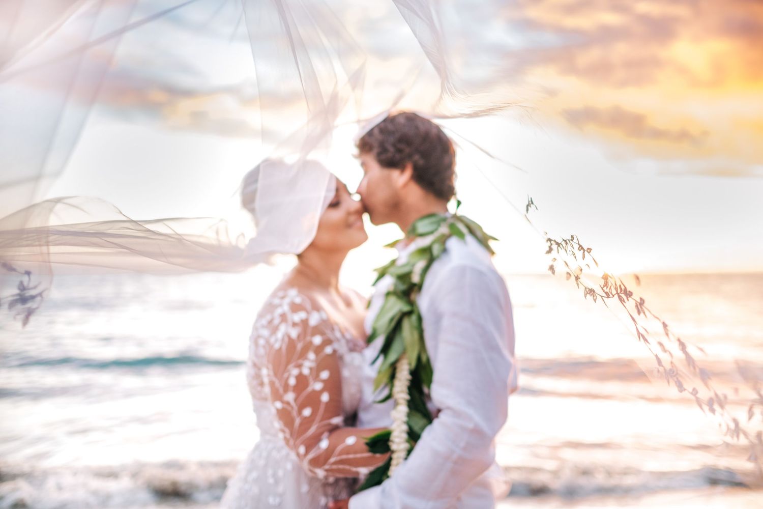 Romantic wedding couple embraces on a beach at sunset with soft pink and orange clouds in the sky. Mauna Kea Beach wedding, Big Island of Ha