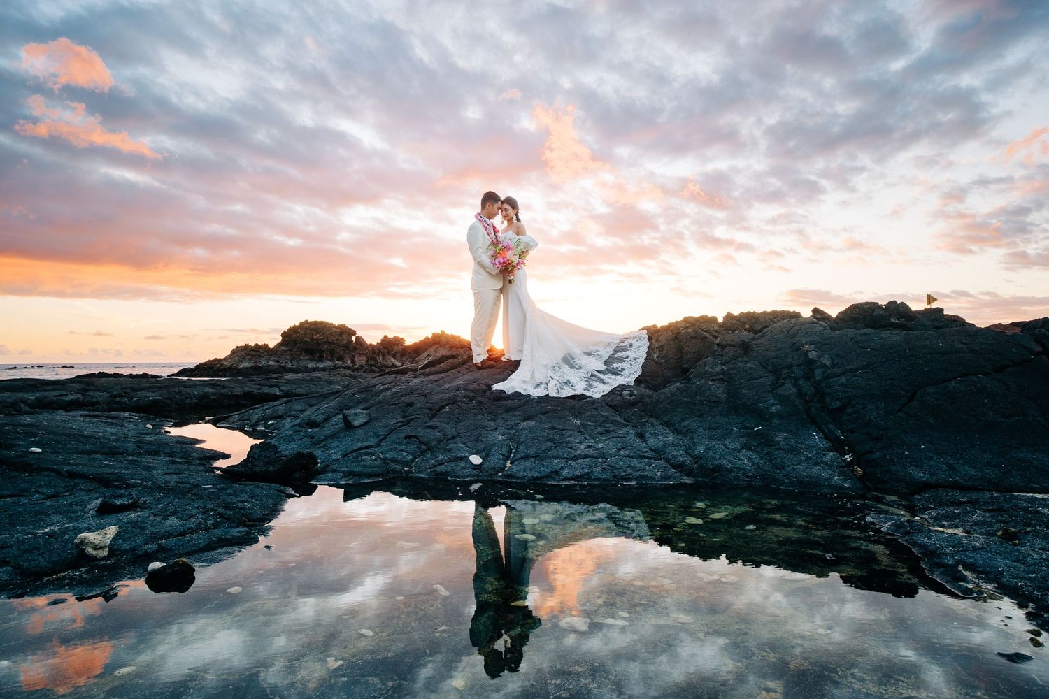 Dramatic sunset sky reflected in tidal pools along a rocky Hawaiian coastline at Kikaua Point Beach, Big Island of Hawaii.