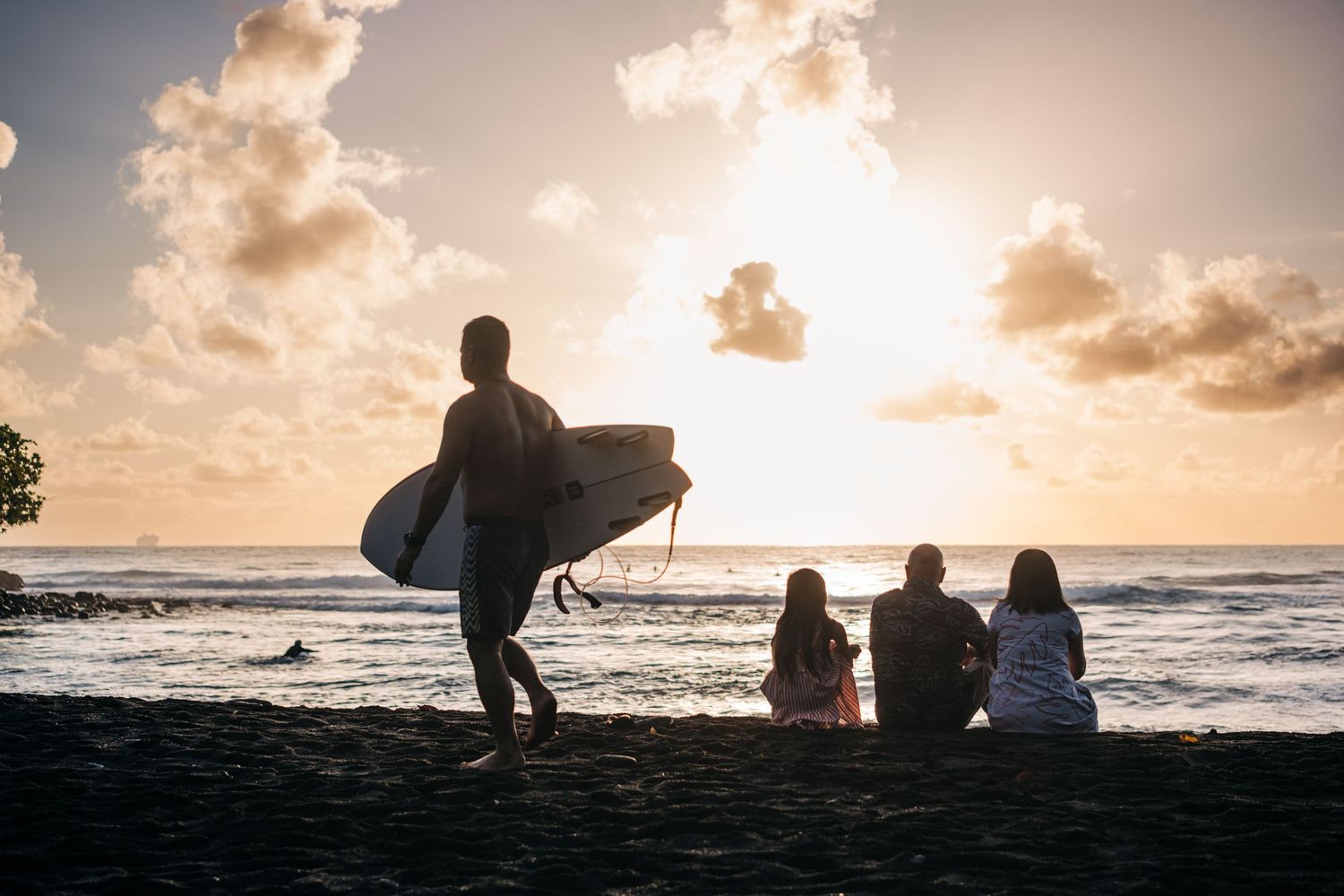 Silhouettes of people sitting on beach watching dramatic sunset over ocean waves in Hilo, Big Island of Hawaii.