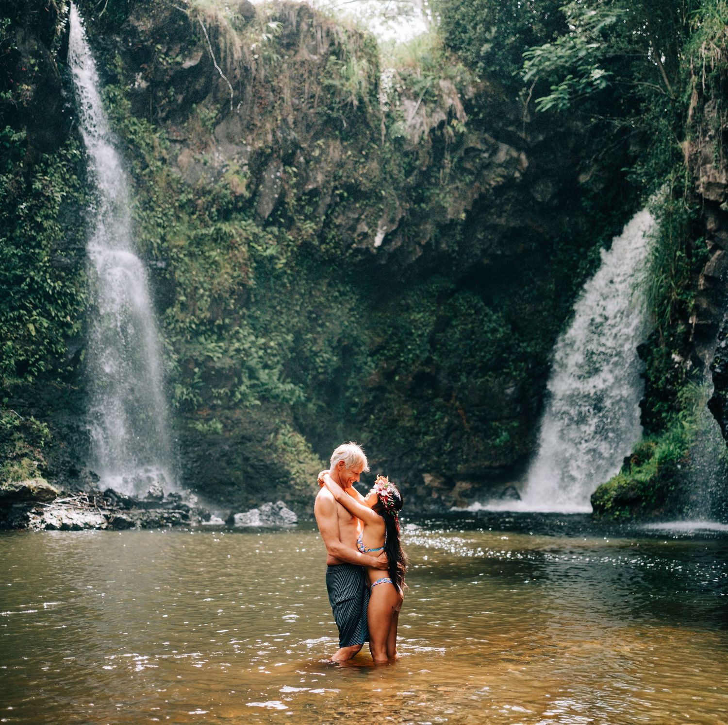 Couple shares romantic moment in natural pool beneath a tropical waterfall in Hilo, Big Island of Hawaii.